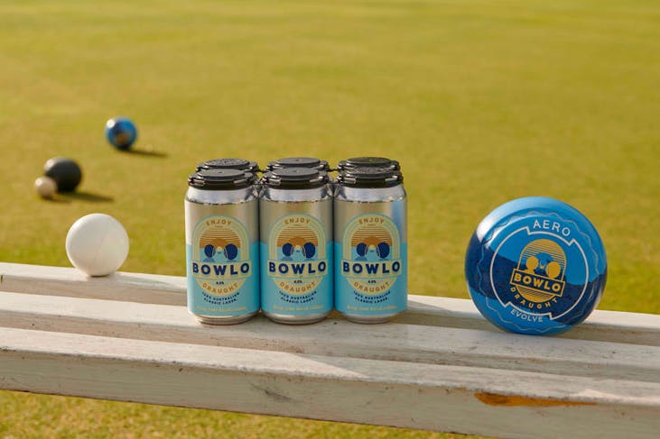 A six-pack of Bowlo Draught with a bowling green in the background.